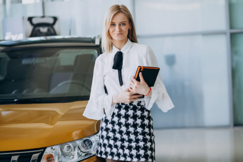 Female salesperson at a car showroom standing by the car